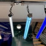 Suspended industrial LED tubular lights in multiple color temperatures and blue illumination, installed in a commercial lighting showroom with clear PC housings