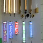 Decorative mesh LED tubular wall lights in gold and black finishes displayed above programmable signage tube lights with EXIT, direction arrows, and commercial graphic inserts