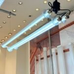 Dual-tube suspended industrial LED tubular light fixture with aluminum connectors, displayed in a showroom alongside clear and frosted tube samples