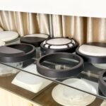 LED bulkhead light housings in various designs, including half-moon covers, grid frames, full diffusers, and black or white round casings displayed on a showroom glass shelf