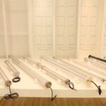 industrial LED tubular light samples, including transparent, frosted, and aluminum-body tubes, shown in front of beam angle distribution charts in a showroom