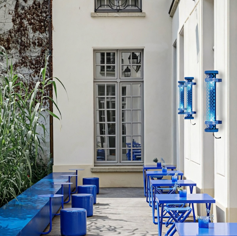 Moreau decorative tubular wall lights installed outdoors, featuring blue metal grille and E27 lamp system in a hospitality courtyard setting